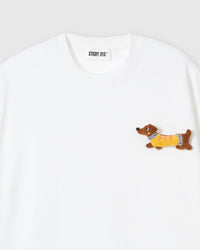 Close-up of plush dachshund applique on white cotton showing stuffed body, yellow sweater, and embroidered face
