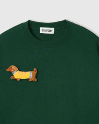 Close-up of plush dachshund applique on forest green cotton showing stuffed body, yellow sweater, and embroidered face