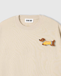 Close-up of plush dachshund applique on cream cotton showing stuffed body, yellow sweater, and embroidered face
