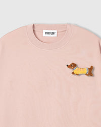 Close-up of plush dachshund applique on pink cotton showing stuffed body, yellow sweater, and embroidered face