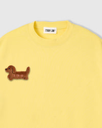 Close-up of hand-stitched plush dachshund applique on lemon cotton tee showing 3D texture and brown plush fur