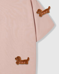 Detail of two plush dachshund appliques on pink cotton showing brown fur texture and placement