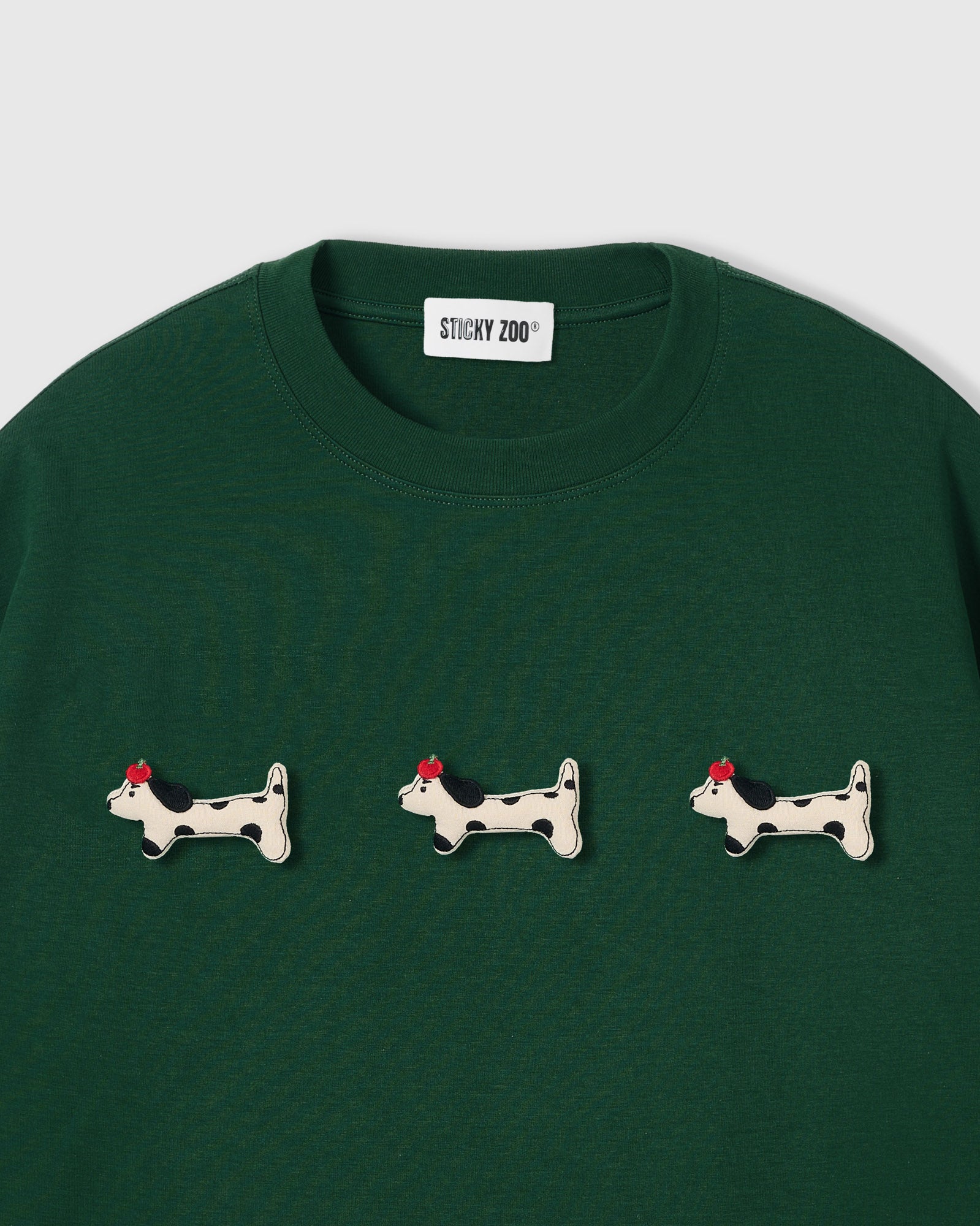 {{Not printed — hand-stitched}} Three plush spotted dachshund appliqués with red beret detail on STICKYZOO green oversized t-shirt