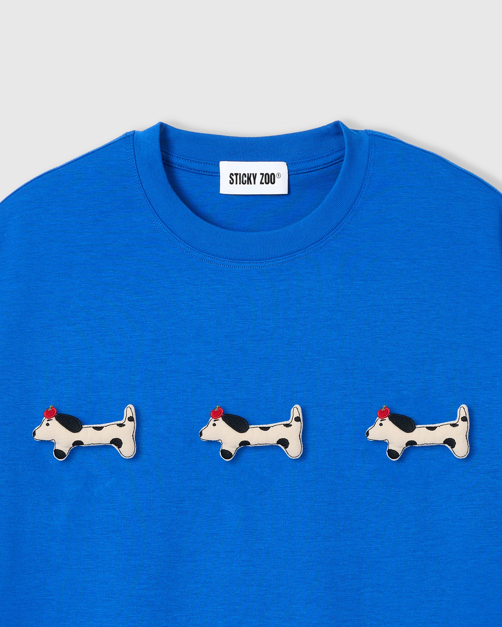 {{Not printed — hand-stitched}} Three plush spotted dachshund appliqués with red beret detail on STICKYZOO blue oversized t-shirt