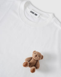 Angled close-up of plush teddy bear on white cotton showing 3D texture with neckline visible