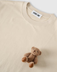 Angled close-up of plush teddy bear on cream cotton showing 3D texture with neckline visible