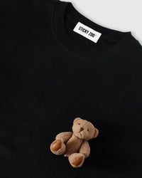 Angled close-up of plush teddy bear on black cotton showing 3D texture with neckline visible