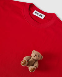 Angled close-up of plush teddy bear on red cotton showing 3D texture with neckline visible