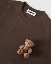 Close-up of plush teddy bear applique showing layered plush construction and leather-tone paw pads on dark brown cotton