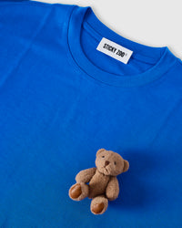 Angled close-up of plush teddy bear on blue cotton showing 3D texture with neckline visible