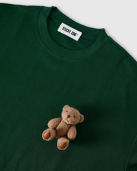 Detail of plush teddy bear near hem on forest green cotton showing hand-stitched construction