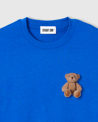Close-up of plush teddy bear with brown fur and stitched paws on royal blue cotton