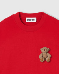 Close-up of plush teddy bear on red 230gsm cotton showing 3D layered texture and embroidered features