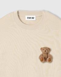 Close-up of full-body plush teddy bear with brown fur and stitched paws on cream cotton