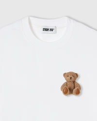 Close-up of full-body plush teddy bear on pure white cotton showing brown fur detail and stitched paws