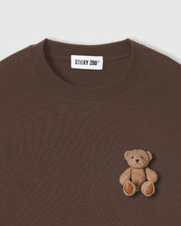 Close-up of hand-stitched plush teddy bear on dark brown 230gsm cotton showing 3D texture and embroidered features