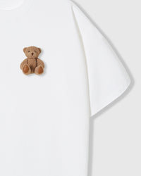 Close-up of seated teddy bear applique on white fabric showing maximum contrast and dimensional texture