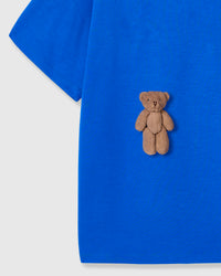 Close-up of seated teddy bear applique showing dimensional texture against blue fabric
