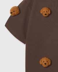 Close-up of shoulder area on brown tee showing plush poodle placement and dropped sleeve