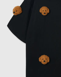 Close-up of shoulder area on black tee showing plush poodle placement and dropped sleeve