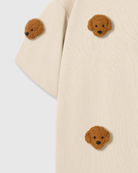 Close-up of shoulder area on cream tee showing plush poodle placement and dropped sleeve