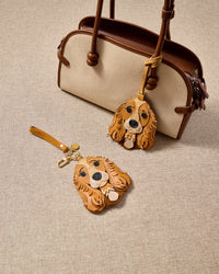 Handmade Cocker Spaniel leather bag charm with keychain clip on a canvas handbag — French Alran leather and suede, 18K gold-plated hardware. STICKYZOO collectible.