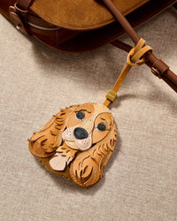 Close-up of handmade Cocker Spaniel leather bag charm clipped to a leather handbag — hand-cut French Alran leather and suede, embroidered eyes, contrast snout. STICKYZOO collectible.