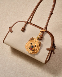 Handmade Chow Chow leather bag charm clipped to a cream canvas handbag — French Alran leather and suede, hand-layered face panels. STICKYZOO collectible.