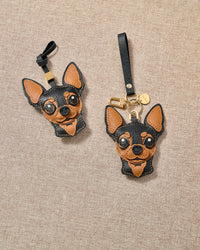 Chihuahua leather bag charm in both attachment formats — leather strap with engraved 18K gold cube and 18K gold-plated keychain clip with engraved gold tag. Handmade French Alran leather and suede.