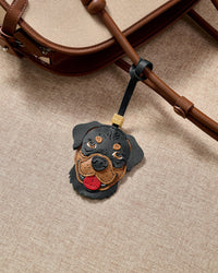 Handmade Rottweiler leather bag charm clipped to a tan textile handbag — French Alran goatskin, 5-day artisan build. STICKYZOO collectible.