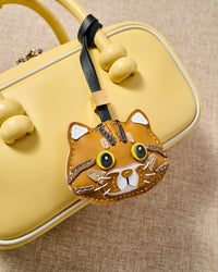 Close-up of the ginger tabby hanging on a pastel yellow bag — genuine French Alran goatskin, never faux, never vegan.