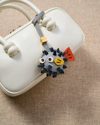 Pufferfish charm styled on a bag, front — a small, specific piece that turns a simple bag into a personal one.