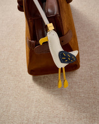 Both editions of the seagull charm — leather strap loop for bags, or 18K gold-plated keychain clip.