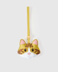 Yellow-strap tabby cat charm handmade from French Alran genuine goatskin — caramel body, brown tabby stripes, pink inner ears, dark eyes, white chin, vivid yellow leather strap. Three days by hand. Arrives in luxury gift packaging. Designed in Amsterdam.