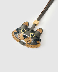 Close-up of the Maison Tabby face, angled — yellow eyes in real leather, warm tan cheek markings, hand-stitched whiskers. Every panel by hand.