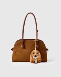 Handmade Cocker Spaniel leather bag charm shown clipped to a brown suede handbag — full-grain French Alran goatskin and suede, hand-layered face panels. STICKYZOO collectible.