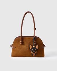 Handmade Chihuahua leather bag charm shown clipped to a brown suede handbag — full-grain French Alran goatskin and suede, hand-layered Applehead face panels. STICKYZOO collectible.