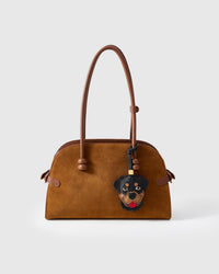 Handmade Rottweiler leather bag charm clipped to a brown suede handbag — French Alran goatskin, 18K gold-plated hardware. STICKYZOO collectible.