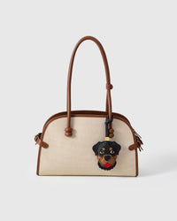 Handmade Rottweiler leather bag charm shown on a cream canvas handbag — hand-layered black and tan French Alran goatskin panels. STICKYZOO collectible.