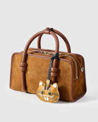 Ginger tabby charm on a brown suede top-handle bag, side angle — real French Alran goatskin, hand-cut over 3 days.