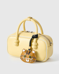Ginger tabby charm styled on a pastel yellow top-handle bag, angled — Real French Alran leather, 3 days by hand.