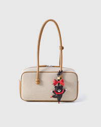 Parisian Bear styled on a cream canvas-and-tan top-handle bag, front — a small, specific piece that changes the whole mood of a bag.