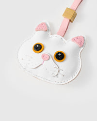 Tight close-up of the snowy cat face — vivid gold-orange eyes in real leather, pink inner ears, pink nose, fine stitched whiskers. Every panel by hand.