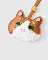 Tight close-up of the patchwork cat face — vivid green eyes in real leather, white face mask, pink heart nose, fine stitched whiskers. Every panel by hand.