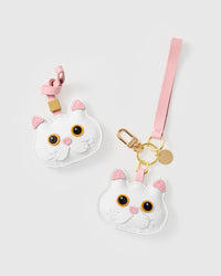 Both editions of the snowy cat side by side — leather strap loop for bags, or 18K gold-plated keychain clip with engraved STICKYZOO disc.