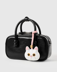 Snowy cat charm on a glossy black box bag, side angle — loved by thousands of cat people. Real French leather, 3 days by hand.