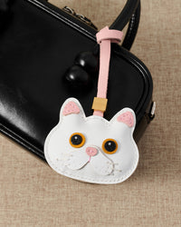 Overhead — snowy cat in strap and keychain editions. Finished one at a time, by hand.