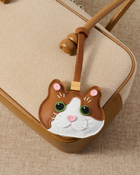 Patchwork cat charm on a tan leather top-handle bag, close detail — real French leather, made to be carried on the bag that sees every day.