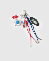 STICKYZOO UFO Odyssey Stack Charm flat lay featuring metallic flying saucer with blue dome, rocket pilot collectible figure, red baseball cap, Keys to the UFO motel tag, and red and blue hand-braided paracord ropes with stainless steel tips