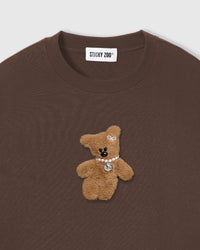 Close-up of plush teddy bear applique on brown cotton showing tonal fur texture and pearl detail
